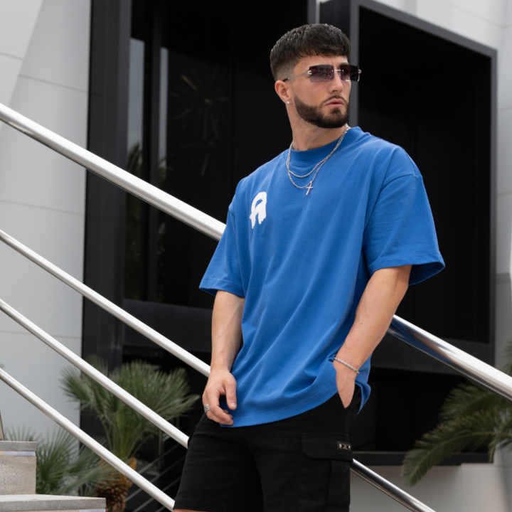Man wearing a blue t-shirt, black shorts, and white sneakers on a modern staircase.
